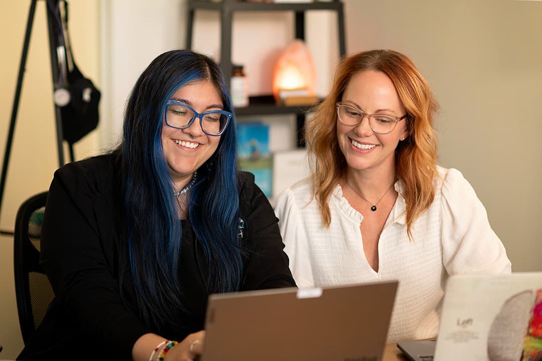 Two members of the Rising Health team smiling as they work together at their laptops